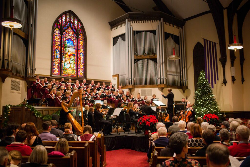 photo of choir singing in Westminster church sanctuary at Christmas time. The sanctuary is decorated with poinsettias and Christmas trees.